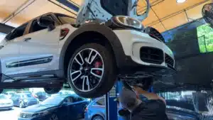 A bright red MINI Cooper sits in a professional auto service bay undergoing scheduled maintenance.