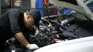 A skilled technician performing routine maintenance on a shiny Mercedes-Benz in a professional service bay.